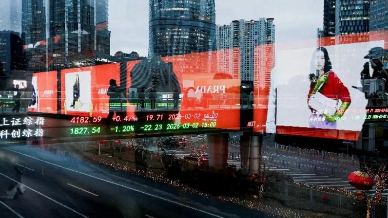 Painel eletrônico mostra os índices de ações de Xangai enquanto as pessoas caminham em uma ponte para pedestres no distrito financeiro de Lujiazui em Xangai, China, em 2 de março de 2026. Foto tirada através de vidro REUTERS/Go Nakamura