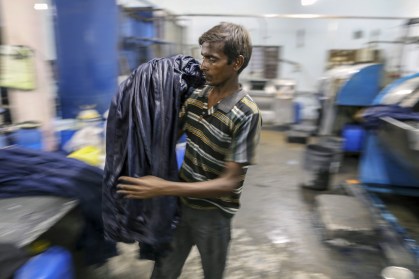 Funcionário descarrega jeans de uma máquina de tingimento de tecidos em uma fábrica na Índia