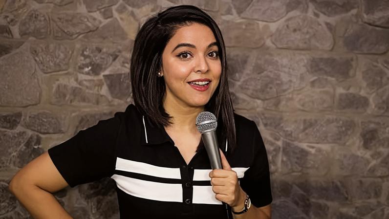 Ankita Shrivastav Ankita Shrivastav, wearing a black-and-white T-shirt, is standing on a stage and holding a mic in her hand.