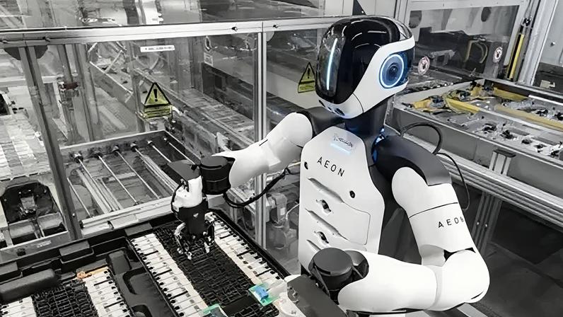 BMW The Aeon robot at work in the factory. It has a white torso with black shoulders. Its black plastic face has a vertical line of blue light.