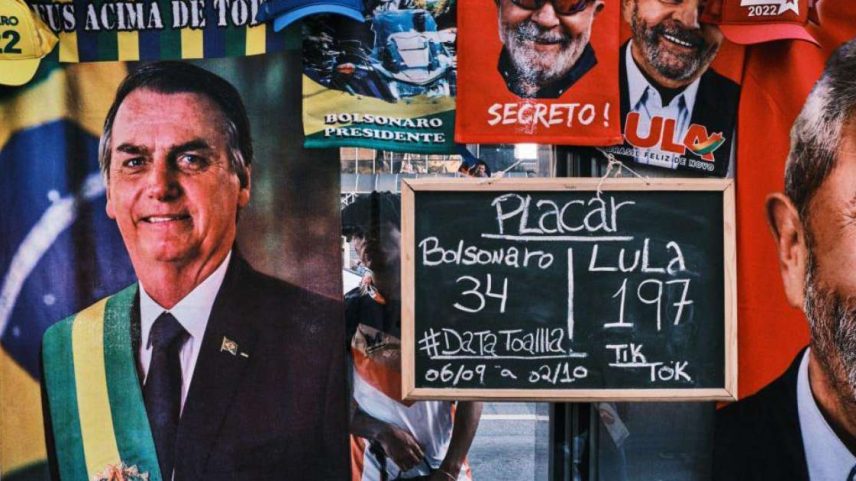 Um homem está em pé ao lado de uma barraca de rua que vende toalhas dos candidatos à presidência Luís Inácio Lula da Silva e Jair Bolsonaro na Avenida Paulista, em 23 de setembro de 2022, em São Paulo, Brasil. A barraca exibe uma placa com o número de toalhas de cada candidato vendidas até o momento.