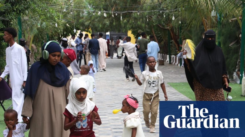 Children with balloons and adults walk on a concrete path surrounded by grass and trees