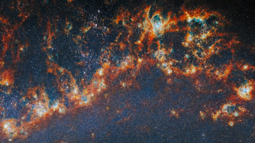 A large, long portion of one of the spiral arms in galaxy M51. Red-orange, clumpy filaments of gas and dust that stretch in a chain from left to right comprise the arm. Shining cyan bubbles light up parts of the gas clouds from within, and gaps expose bright star clusters in these bubbles as glowing white dots. The whole image is dotted with small stars. A faint blue glow around the arm colors the otherwise dark background.