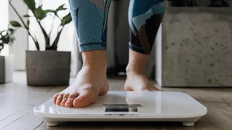 Getty Images A woman in gym clothing steps on to electronic weighing scales at home