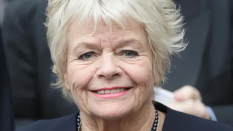 Judith Chalmers smiling in a navy blue blazer and necklace in 2016