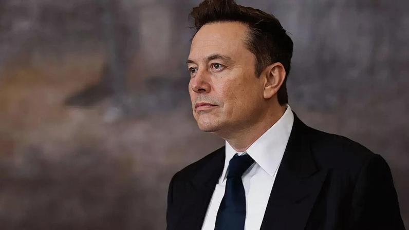 Elon Musk vestindo um terno preto, camisa branca e gravata preta olhando para longe