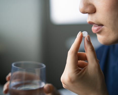 A woman holding a glass of water in one hand pops a pill into her mouth with her other hand