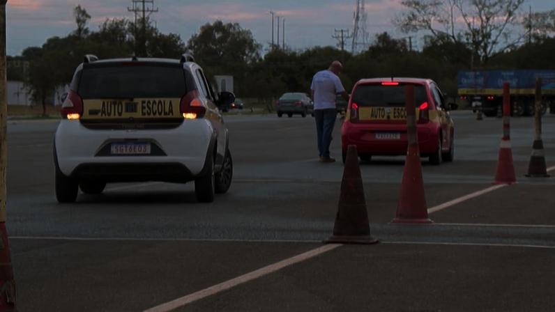 Carros de autoescola em pista de treino, com cones de sinalização e instrutor ao lado do veículo