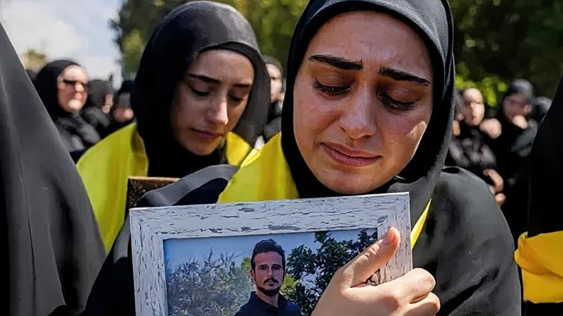 A woman wearing a black hijab mourns a relative killed in an Israeli air strike, while clutching a portrait of the victim (22/04/26)