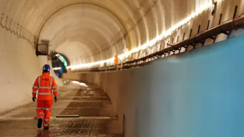PA Media A man in hi-vis clothing, branded with the logo of HS2, walks through the Chilterns tunnel