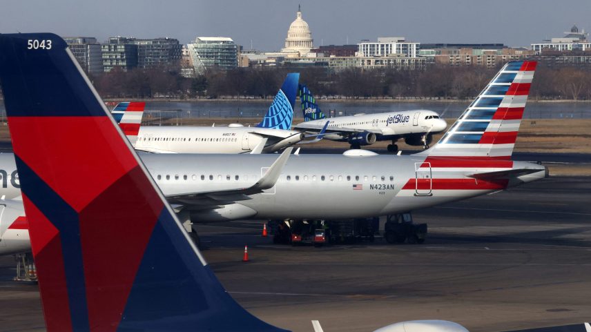 A JetBlue aircraft lands under the DC skyline featuring the U.S. Capitol building, near United Airlines, American Airlines and Delta Airlines aircraft on the tarmac at Ronald Reagan Washington National Airport in Arlington, Virginia.