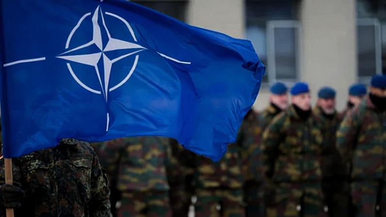 Imagem de vários soldados enfileirados, com um soldado a frente, segurando a bandeira da Otan - Metrópoles