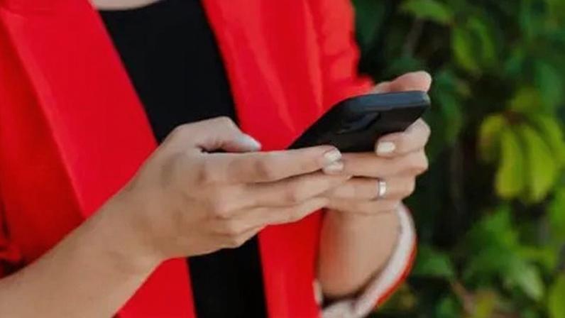 Getty Images Close up of a woman's hands holding a black smartphone. She is wearing a bright red jacket and a silver ring.