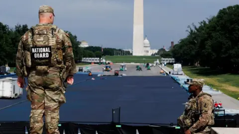 EPA Two National Guards men in camouflage uniforms watch workers and trucks in the drained Lincoln Memorial reflecting pool, which is partially painted blue. The Washington Monument and the Capitol building are in the background