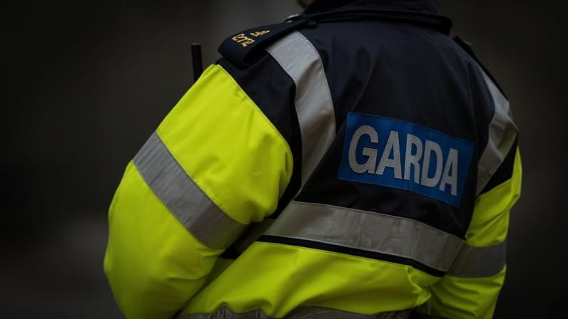 The back of a gardaí uniform raincoat. Garda is wrriten in white and blue, and the rest of the coat is a reflective neon yellow colour with silver stripes on the arms and chest area.
