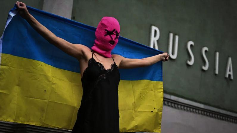 Uma integrante do coletivo ativista Pussy Riot segura uma bandeira ucraniana durante um protesto contra a participação da Rússia na Bienal de Veneza, em frente ao pavilhão russo, em 6 de maio de 2026, em Veneza.