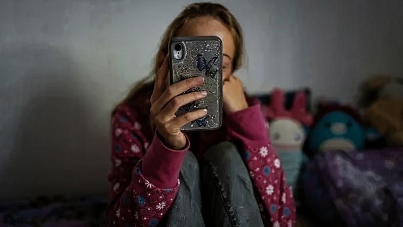 Getty Images A anonymous young girl looking at her phone on her bed in a room with brightly coloured cuddly toys. She is wearing a pink flowery jumper and jeans, we cannot see her face.