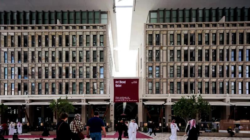 People walk in front of a building labeled "Art Basel Qatar"