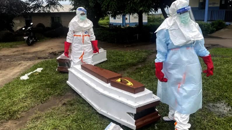 Profissionais da saúde ao lado de caixão de vítima de Ebola no Congo