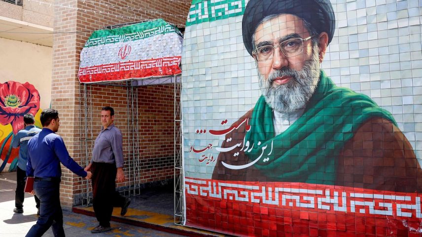 Pessoas caminham pelas ruas de Teerã e passam por banner com imagem do aiatolá Mojtaba Khamenei.