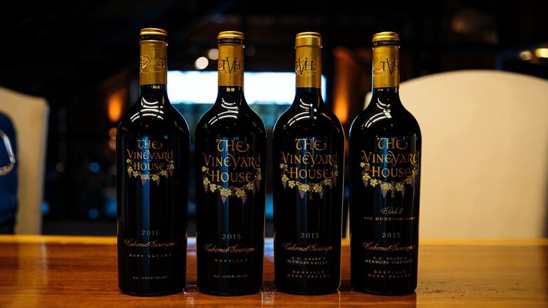 Four bottles of red wine with gold tops, with 'The Vineyard House' on the label