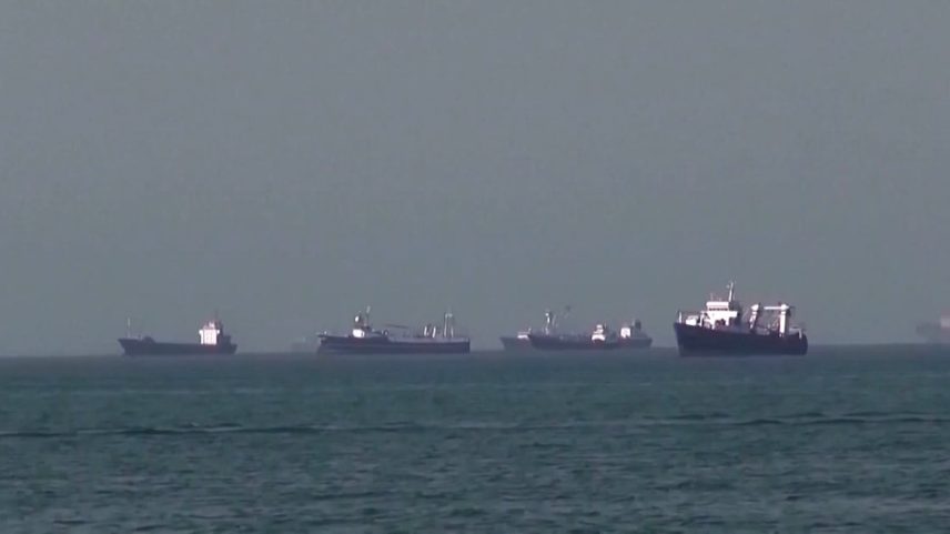 Navios cargueiros alinhados no horizonte em mar calmo sob céu nublado em Ormuz