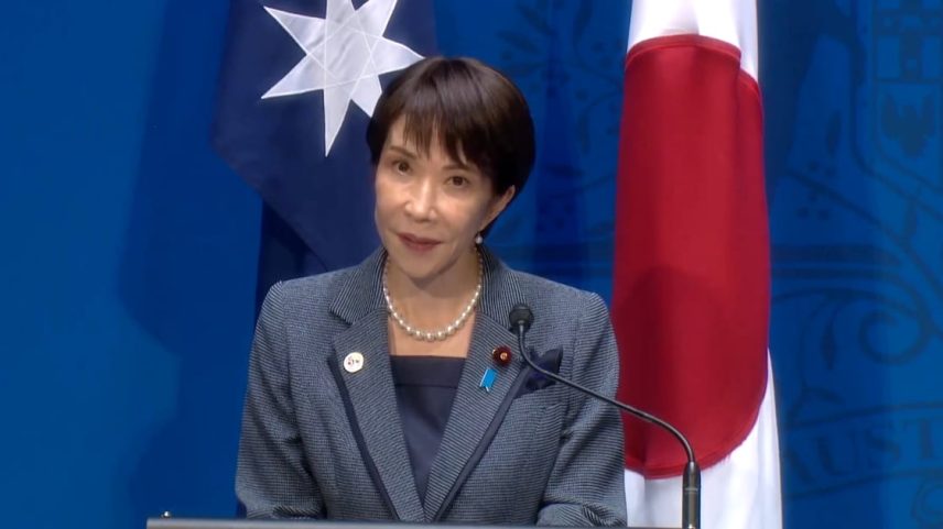 A primeira-ministra do Japão, Sanae Takaichi, discursa em frente a uma bandeira australiana e outra japonesa.