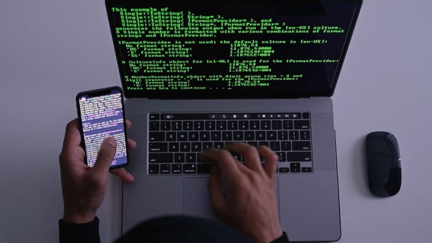 Uma pessoa suspeita de identidade não revelada acessa uma tabela de códigos em um laptop e digita sequências observadas na tela de um celular.