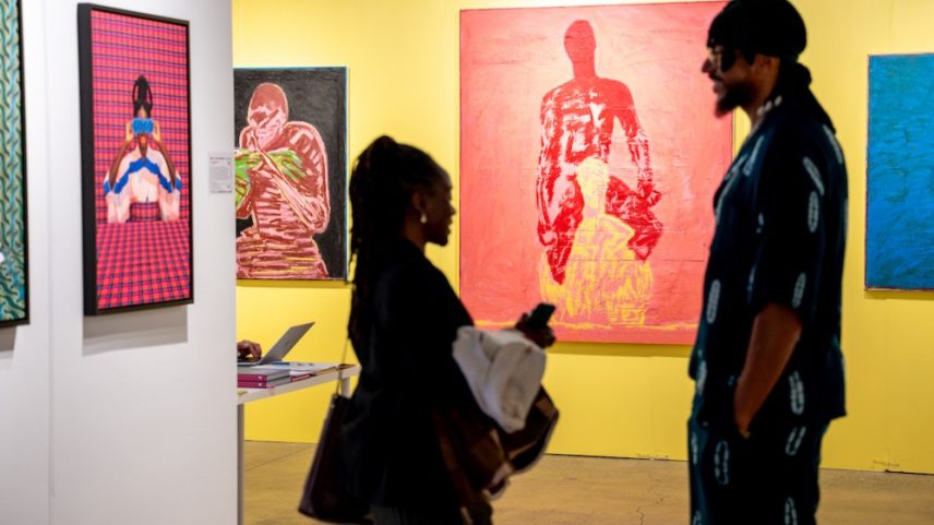 Two figures standing in the midst of colorful paintings.