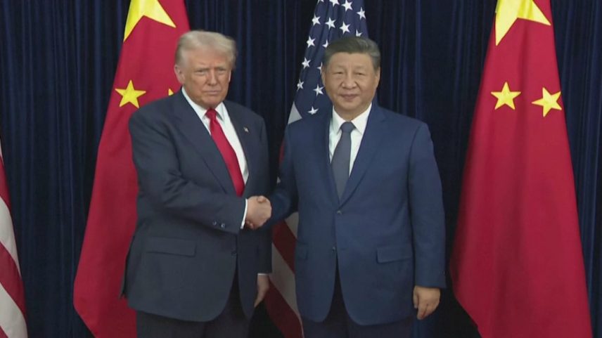 O presidente dos EUA e da China estão lado a lado, dando um forte aperto de mão. Atrás deles, é possível observar bandeiras de seus respectivos países.