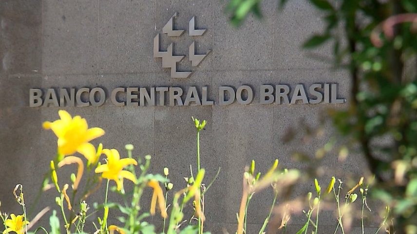 Fachada do Banco Central do Brasil com flores amarelas em primeiro plano
