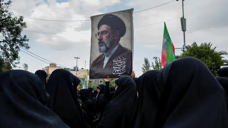 Imagem de uma mulher segurando uma foto de Mojtaba Khamenei, líder supremo do Irã, em cerimônia em memória a vítimas da guerra, em Teerã, Irã, no domingo, 24