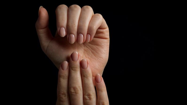 Mãos femininas em um fundo bege. Nas unhas, esmalte em gel nude