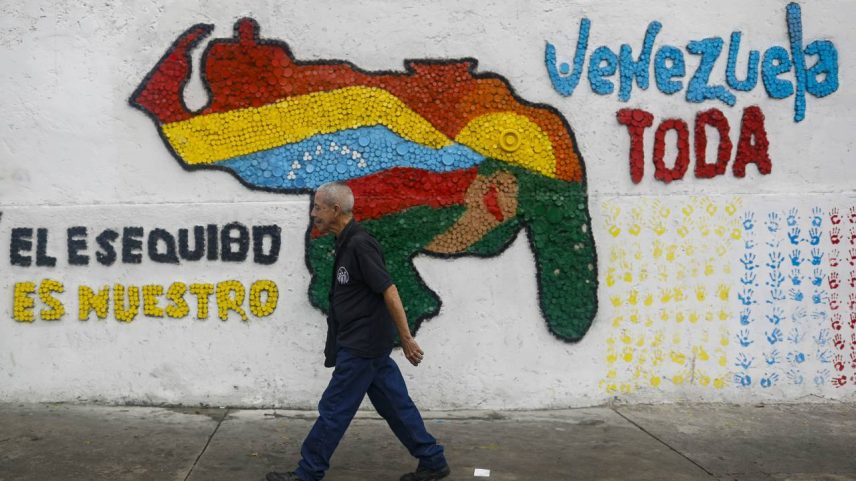 Um homem caminha ao lado de um mural com o mapa da Venezuela que inclui o território de Essequibo, em Caracas, Venezuela