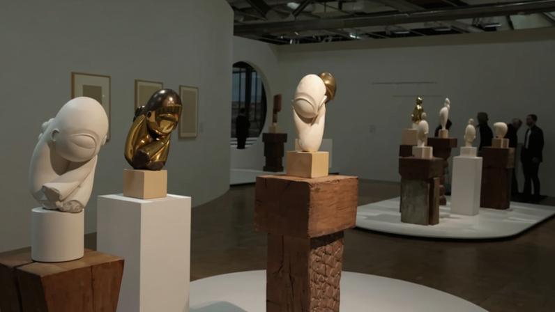 A group of spare sculptures of human heads on wooden pedestals in a gallery.