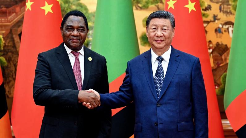 Hakainde Hichilema and Xi Jinping shaking hands in front of both countries flags