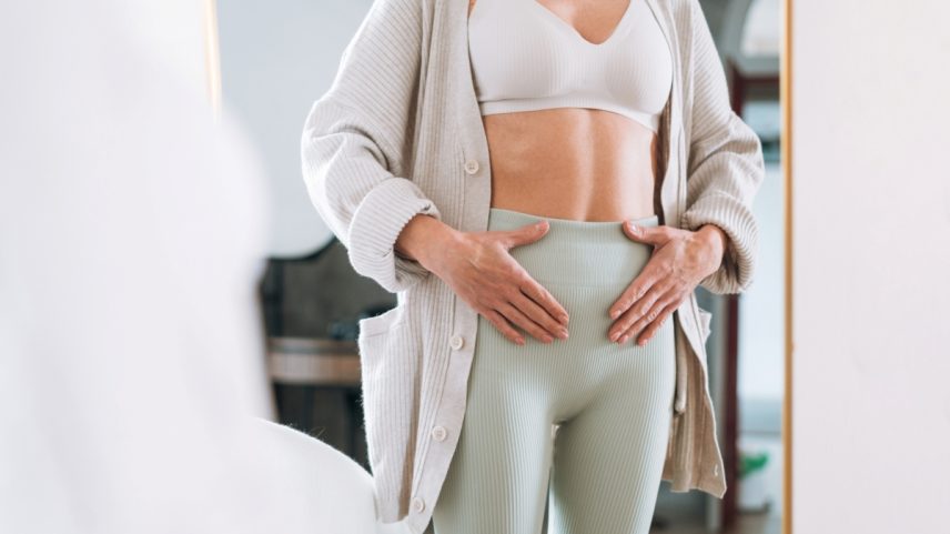 Woman Holding Lower Abdomen at Home, Portraying Self-Care During Menstrual Pain or Bloating Discomfort