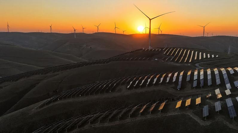 Em uma vista aérea, o brilho do pôr do sol ilumina turbinas eólicas e fileiras de painéis solares em um parque de energia eólica em 28 de outubro de 2025, em Qingyang, na província de Gansu, China