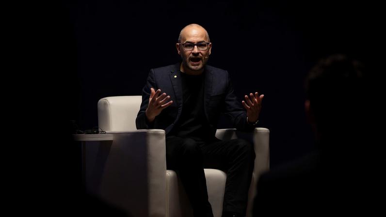 Demis Hassabis speaks while seated on a stage