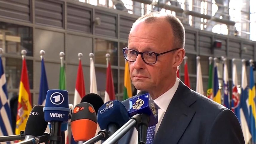 O premier alemão Friedrich Merz é entrevistado por dezenas de jornalistas em um salão aberto adornado com as bandeiras de dezenas de países europeus.