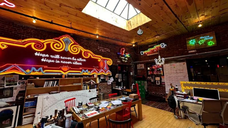 View of a studio with various neon works all around and a skylight above.