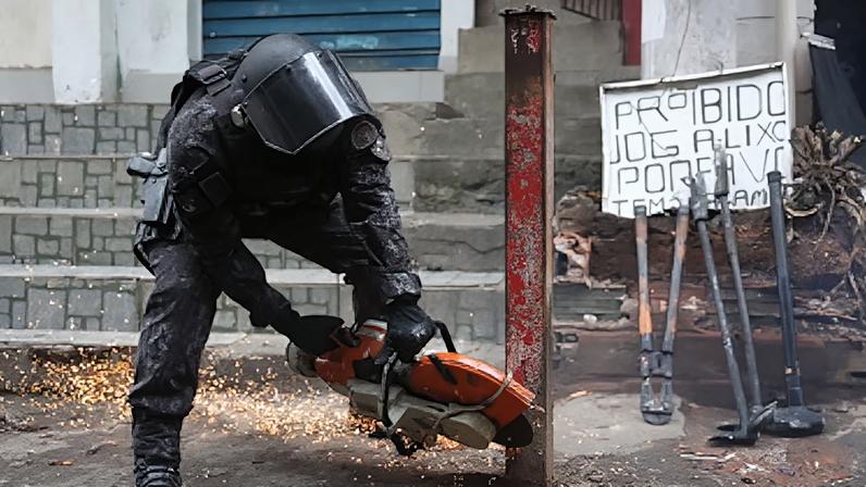 Policial da Tropa de Choque corta parte de bloqueio de metal em Paraisópolis