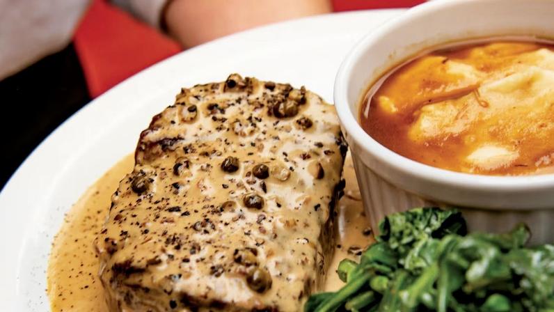 Filé mignon ao molho poivre com purê de batatas e espinafre ao lado sobre prato.