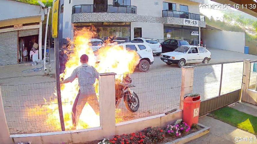 Pessoa em chamas ao lado de uma motocicleta pegando fogo em frente a um prédio