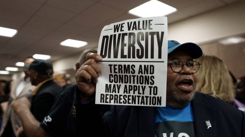 Homem segura cartaz durante audiência pública sobre redistribuição de distritos, em Baton Rouge, Louisiana, EUA - 08/05/2026 (Foto: REUTERS/Wayan Barre)