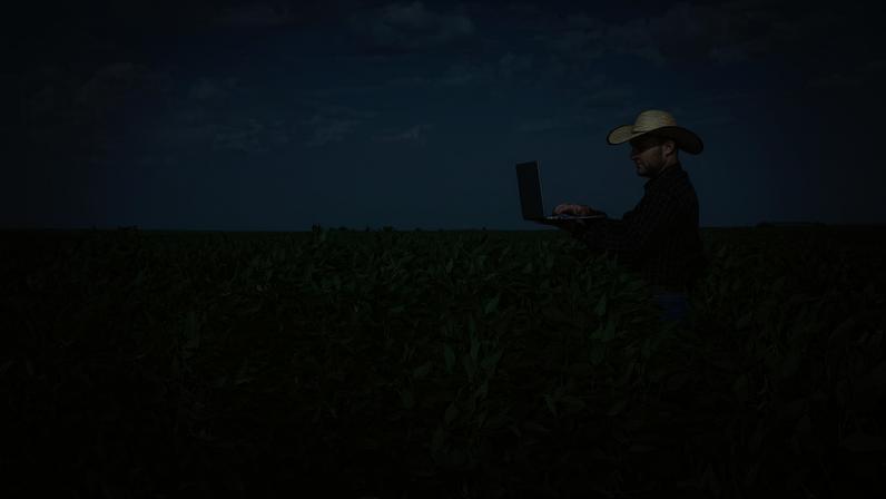 Imagem de um produtor rural usando um notebook na lavoura.
