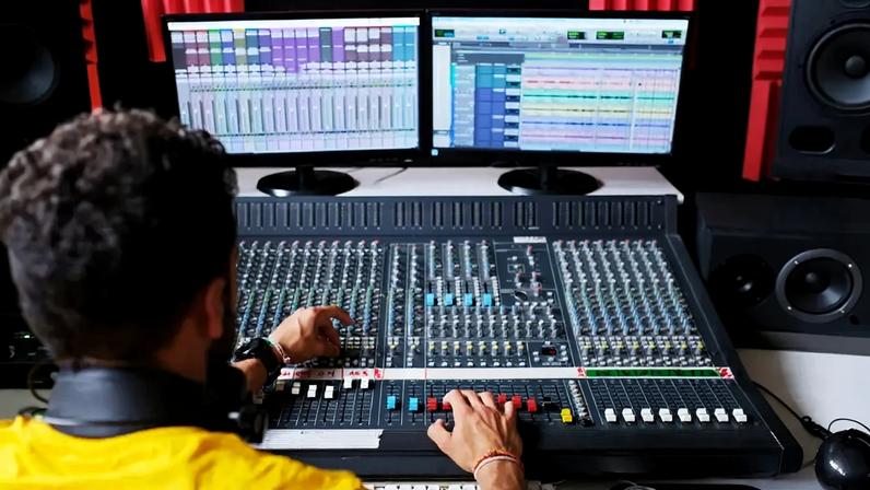 Imagem de um rapaz controlando uma mesa de som numa emissora de rádio.