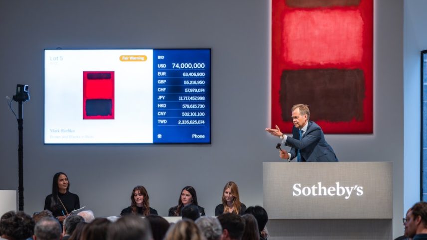 A man in a suit at a rostrum before a red abstract painting.