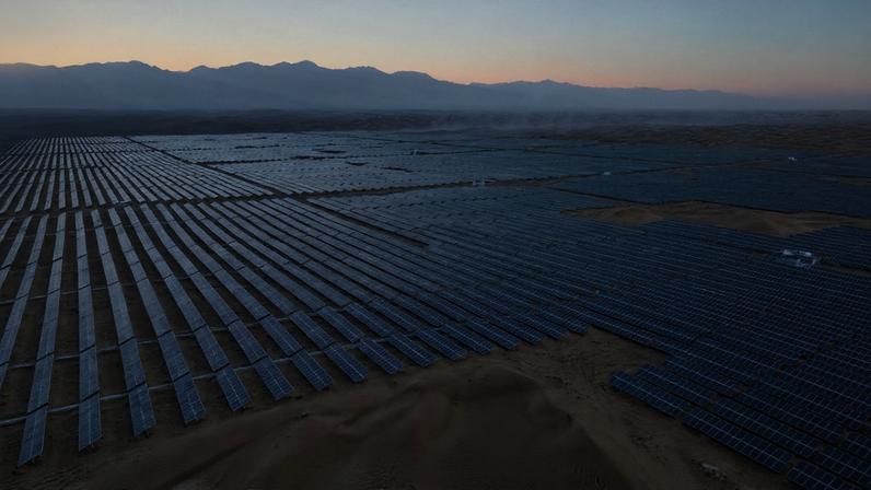Fileiras de painéis solares avançam sobre o solo seco do deserto