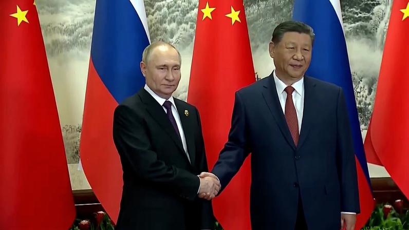 Vladimir Putin e Xi Jinping apertando as mãos diante de bandeiras da China e da Rússia